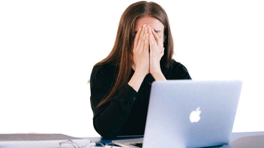 A person sitting in front of a laptop with their hands covering their face, showing signs of frustration or disappointment, likely after failing an exam